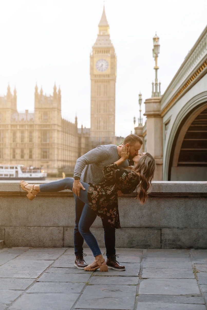 a man and woman kissing in front of a clock tower